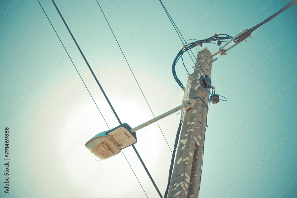 Obraz premium Low angle view of utility pole with electrical wires and a streetlight against a clear sky
