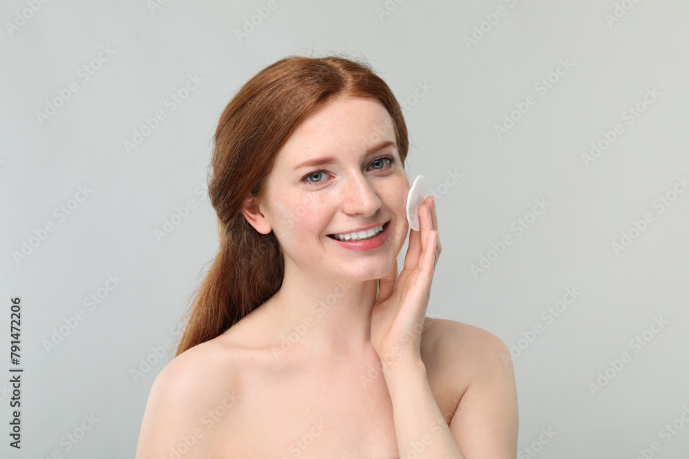 Smiling woman with freckles wiping face on grey background Smiling woman with freckles wiping face on grey background