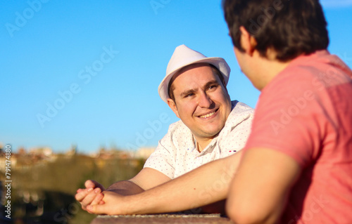 Couple of gay men looking at each other in a lookout point holding hands with the sky in the background, image with copy space. LGBT couple concept