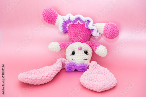 Bunny. Hobby crochet. Handmade. Amigurumi. Pink knitted rabbit. Soft toy. Long ears. Pink background. Crocheting of soft toys