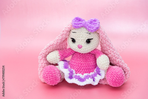 Bunny. Hobby crochet. Handmade. Amigurumi. Pink knitted rabbit. Soft toy. Long ears. Pink background. Crocheting of soft toys