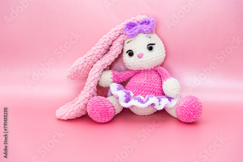 Bunny. Hobby crochet. Handmade. Amigurumi. Pink knitted rabbit. Soft toy. Long ears. Pink background. Crocheting of soft toys