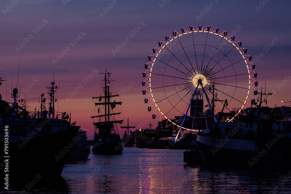 SEA PORT - A small tourist ship in  harbor at dusk against background of ferris wheel 
