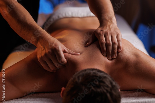 Physiotherapist massaging male patient with damaged shoulder muscle, treating sports injuries. Relaxing professional shoulder massage in cozy atmosphere, reboot on the weekend, end of difficult week.