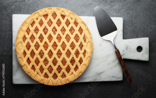 Crostata, orange jam tart and marble cutting board with cake scoop isolated on gray background, top view, flat lay.