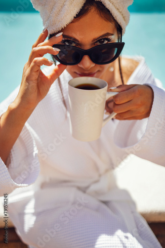 Young pretty woman in a white bathrobe holds a cup of coffee.