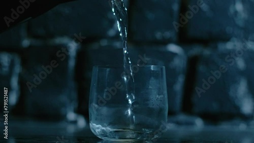 Hot water falling into a drinking glass, close up motion. Dark background with splashing falling water, night drinking wake up photo