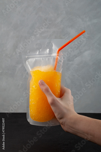 Adult citrus drink in reusable pouch with drinking straw in woman's hand. Orange wine slushy. Alcohol cocktail in spill-proof plastic bag. Refreshing summer take away drink