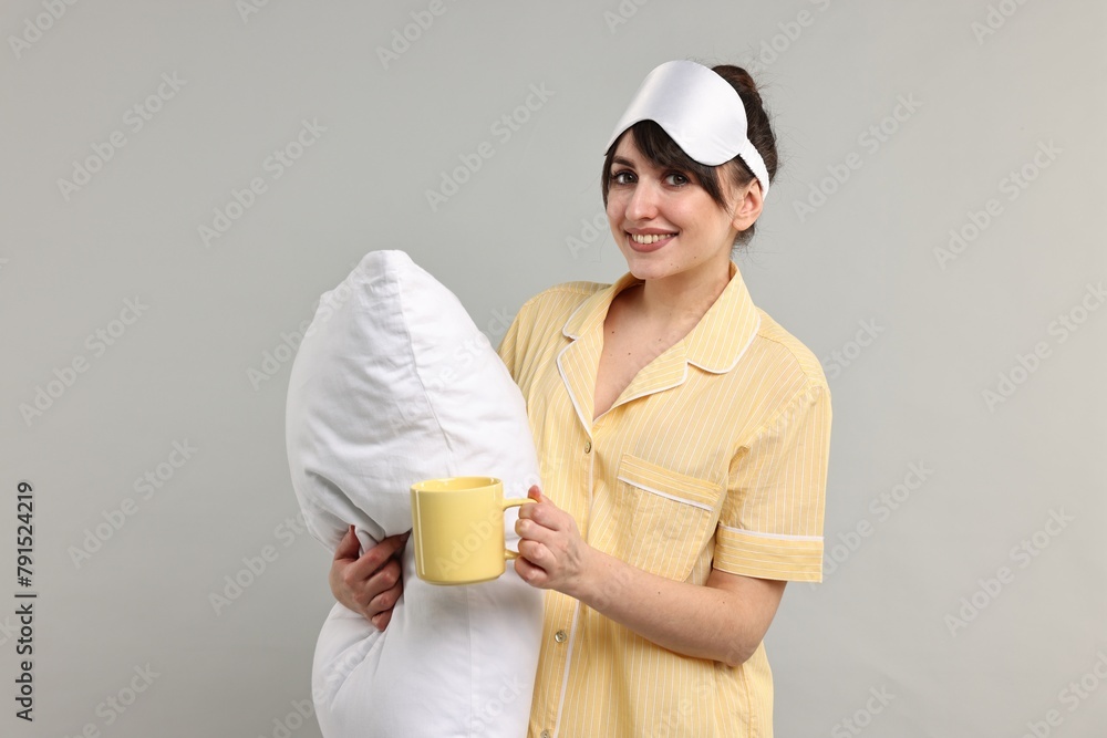 Happy woman in pyjama holding pillow and cup of drink on grey background Happy woman in pyjama holding pillow and cup of drink on grey background