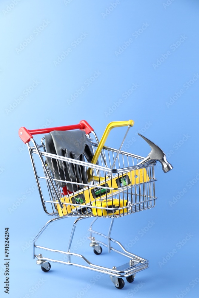 Small shopping cart with set of construction tools and gloves on light blue background Small shopping cart with set of construction tools and gloves on light blue background