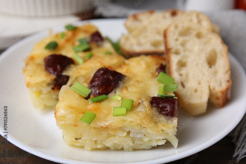 Tasty sausage casserole with green onion and bread on table, closeup