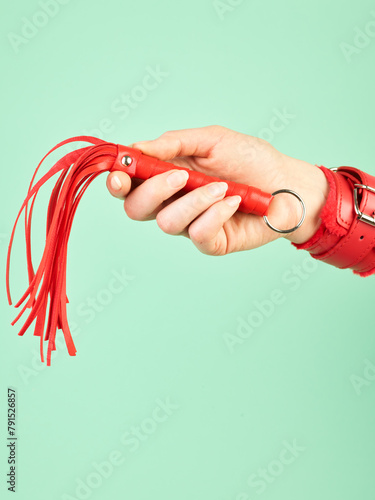 Woman's hand holding red whip for adult role play games over mint background