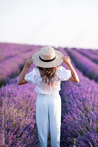 Kid girl 14-15 year old wearing straw hat standing in blooming lavender field outdoor. Summer vacation season.