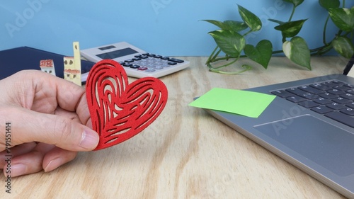 Man's hand holds a cloth heart, on the office desk with computer and calculator.