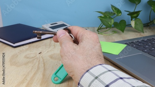 Man's hand holds a door key, on office desk with agenda, computer.