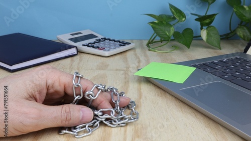 Man's hand holds a metal chains, on the office desk with computer and agenda.