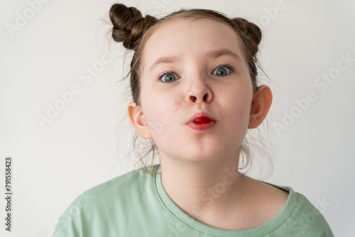 Funny little girl fooling around while holding a red lollipop in her mouth.