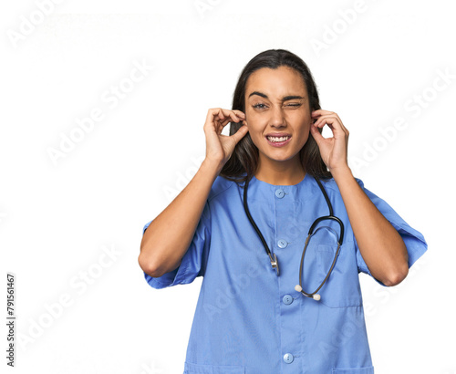 Hispanic nurse in uniform with stethoscope covering ears with hands.