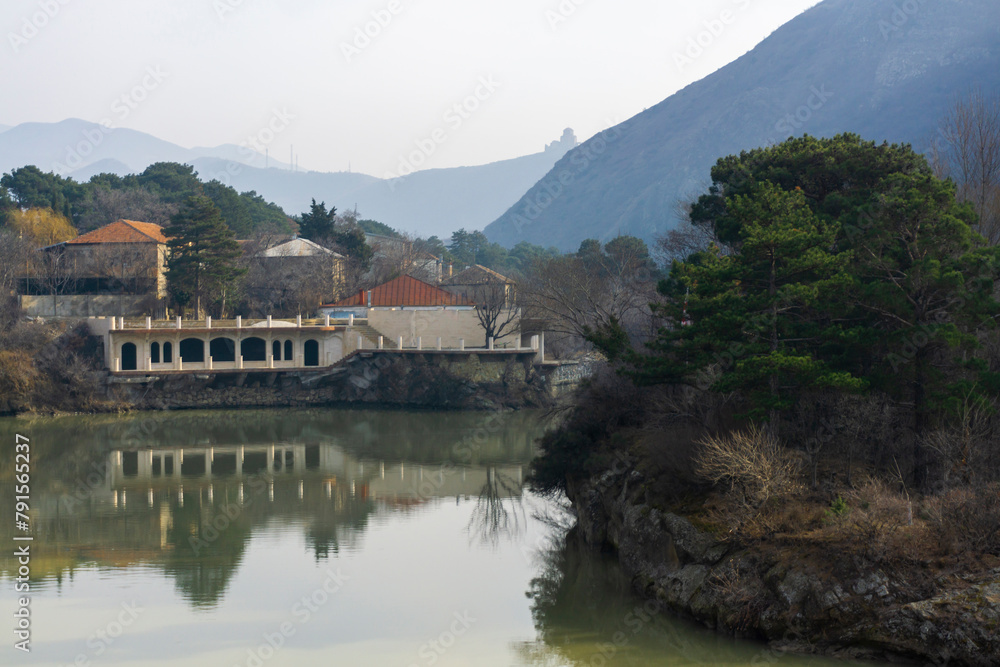 View of the Mtkvari (Kura) river from the bridge in the city of Mtskheta. High mountain and Jvari monastery on the hill. Reflection of the sky, buildings and trees in the water.