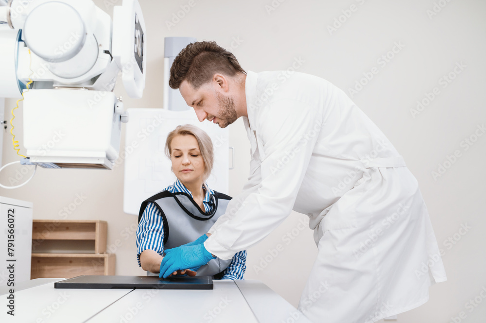Obraz premium A male doctor places the hand of a female patient to take an x-ray on a special stand in an office with an x-ray machine, medical equipment.