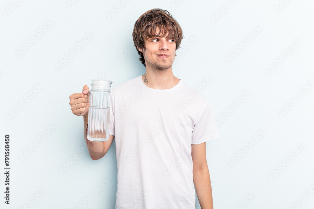 Young caucasian man holding a jar of water isolated on blue background confused, feels doubtful and unsure. Young caucasian man holding a jar of water isolated on blue background confused, feels doubtful and unsure.