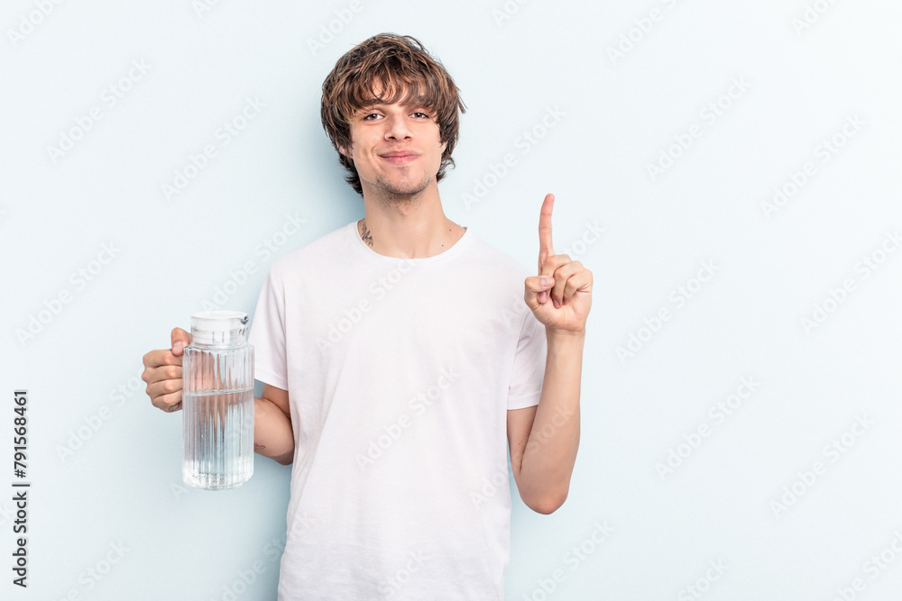 Young caucasian man holding a jar of water isolated on blue background showing number one with finger.