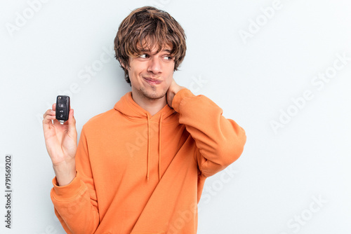 Young caucasian man holding car keys isolated on blue background touching back of head, thinking and making a choice.