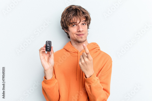 Young caucasian man holding car keys isolated on blue background pointing with finger at you as if inviting come closer.