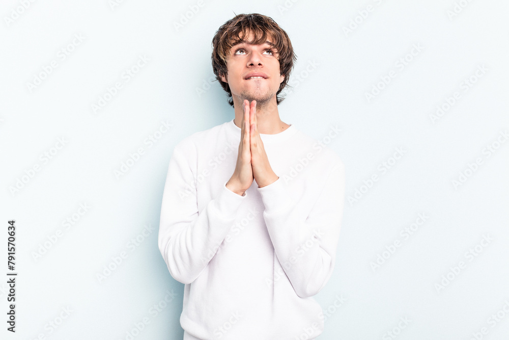 Young caucasian man isolated on blue background holding hands in pray near mouth, feels confident. Young caucasian man isolated on blue background holding hands in pray near mouth, feels confident.