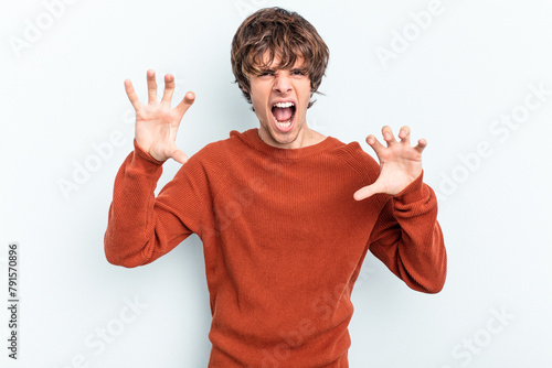 Young caucasian man isolated on blue background showing claws imitating a cat, aggressive gesture.