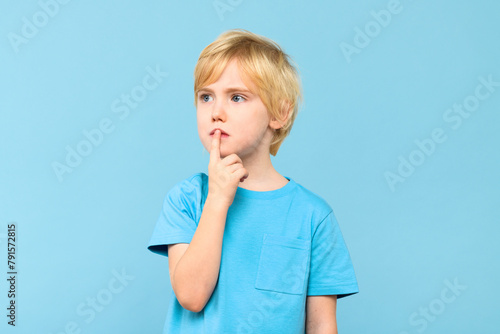Young pensive boy, trying to find solution to a problem, studio portrait isolated on pastel blue background.