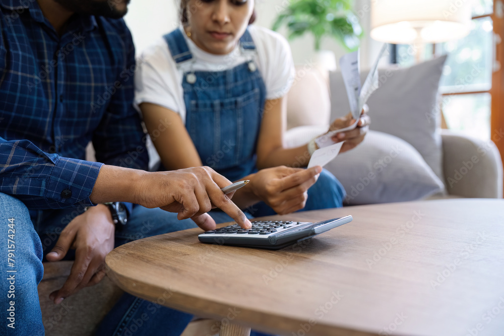 Indian married couple calculating bills, discussing planning budget together, serious wife and husband looking at calculator, checking finances Indian married couple calculating bills, discussing planning budget together, serious wife and husband looking at calculator, checking finances