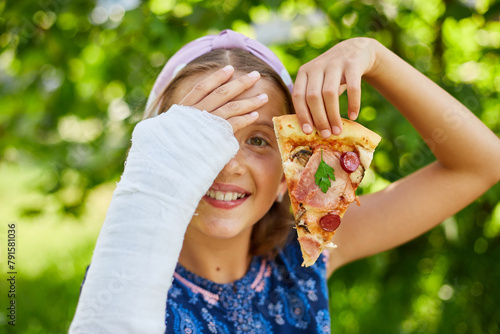 Smiling Young Girl With Cast Enjoying Pizza Outdoors on a Sunny Day