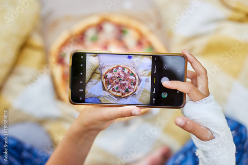 Person With a Cast on Their Arm Taking a Smartphone Photo of Pizza