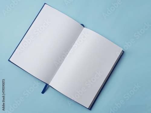 Open empty white paper book laying on blue desk, top view flat lay angle