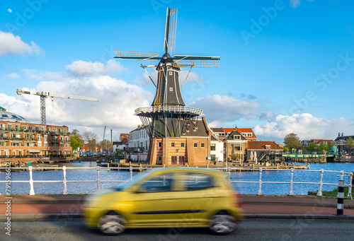 Beautiful dutch scenery, car passing by traditional dutch windmill in Haarlem on a sunny spring day