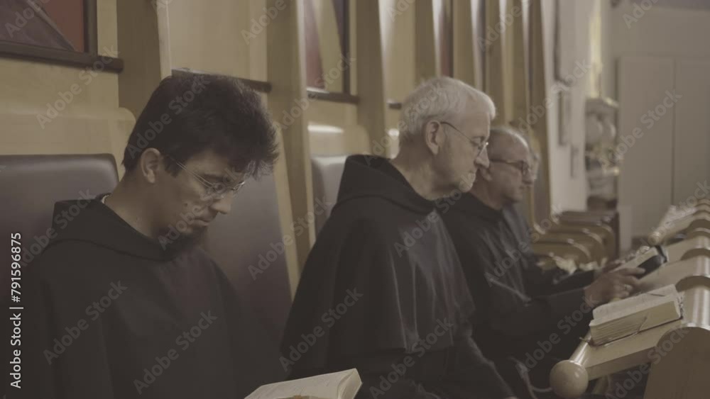 Monks reading Bible together while sitting in church side view medium shot. Christian monks praying liturgy with psalmbook. Liturgy of the Hours concept Monks reading Bible together while sitting in church side view medium shot. Christian monks praying liturgy with psalmbook. Liturgy of the Hours concept