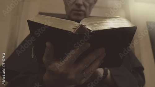 Christian monk in robe reading bible close up. Catholic church priest standing up with psalmbook in hands, low angle view photo