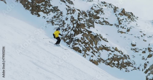 Freeride skier descending a steep mountain turning and spraying powder snow. Skier descends a steep snowy mountain slope and splashes of powder snow around him