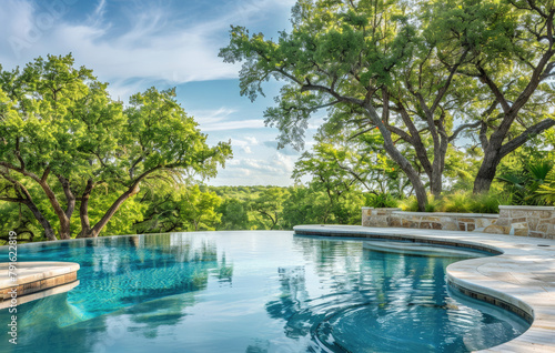 A large, simple pool in the backyard of an upperclass home with a concrete patio and trees and a blue sky photo