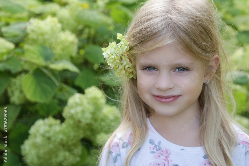 Candid outdoor portrait of happy little girl with green flower behind her ear