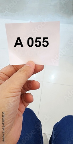 Hold queue card number A 055 with numbers printed in black on white paper. paper queue from the machine waits for a transaction, such as  pay bills or depositing cash in a bank, service center, govern