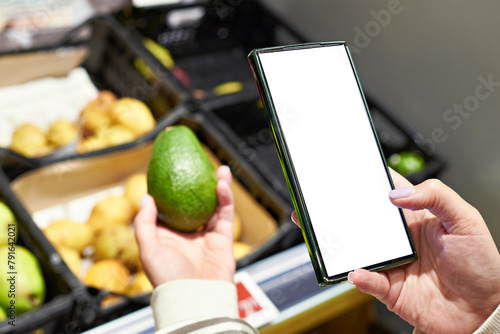 Avocado fruit in hand and smartphone isolated white