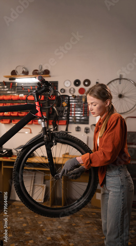 Beautiful female worker repairing bicycle. Bike workshop or garage interior.