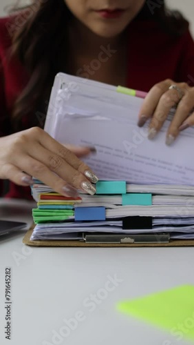 A woman doing paperwork is searching for a sheet of paper in a pile of documents on her desk.