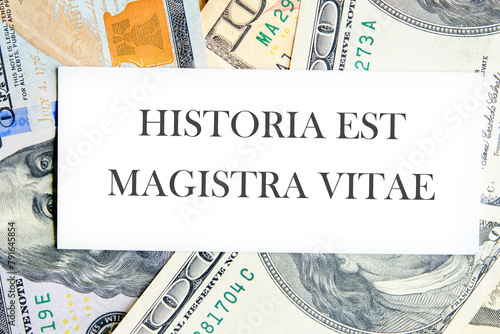 Historia est vitae magistra (History is the tutor of life) Latin phrase on a white business card lying on dollars photo