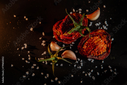 Slices of sun-dried tomatoes on black background with spices and salt