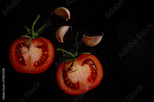 Slices of fresh tomatoes on black background with garlic