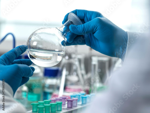 Gloved hands handling a round laboratory flask.