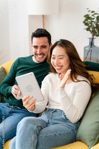 Couple laughing and holding a tablet on a couch. photo